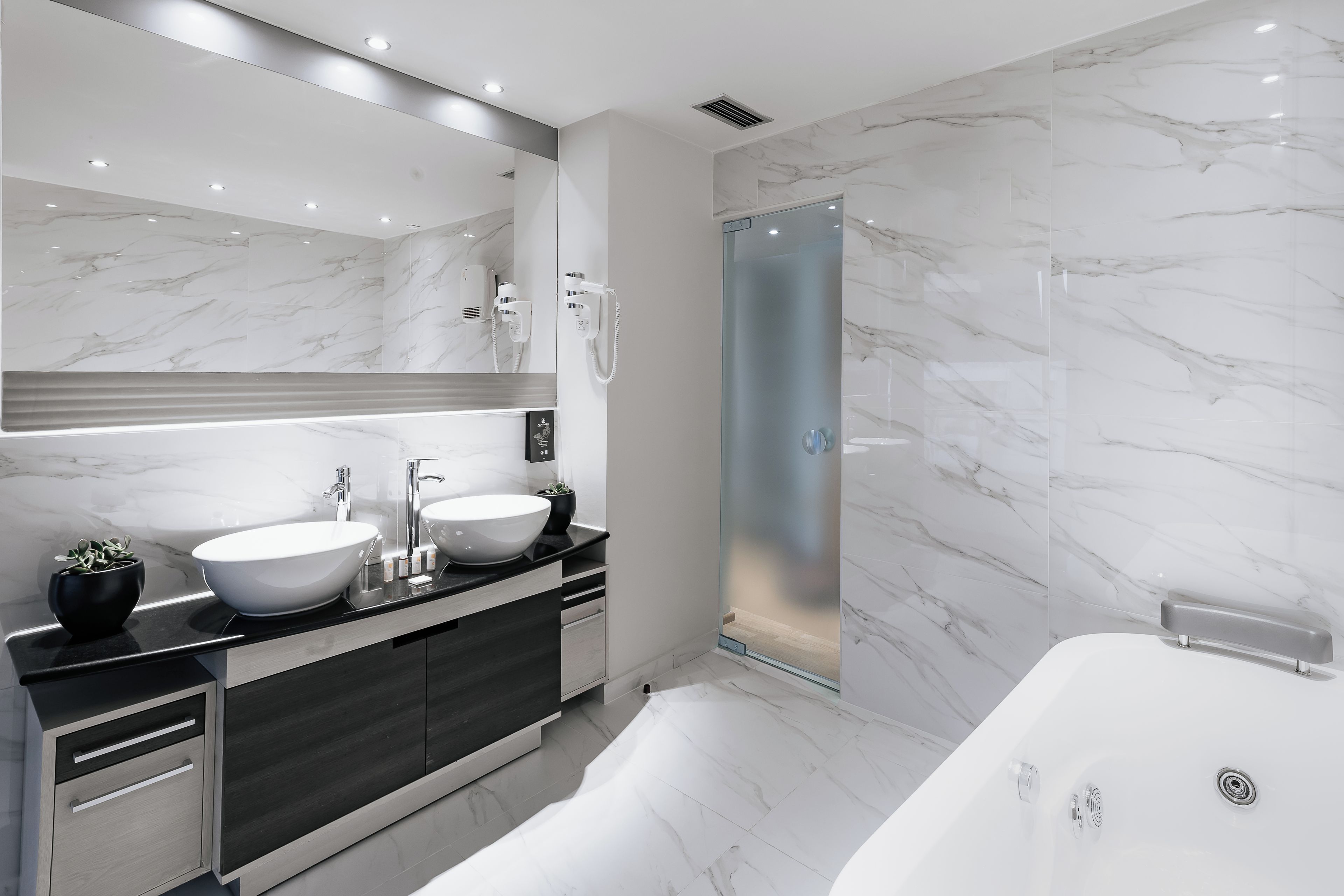 Un baño moderno con dos lavamanos, un espejo grande, ducha a pie y bañera.