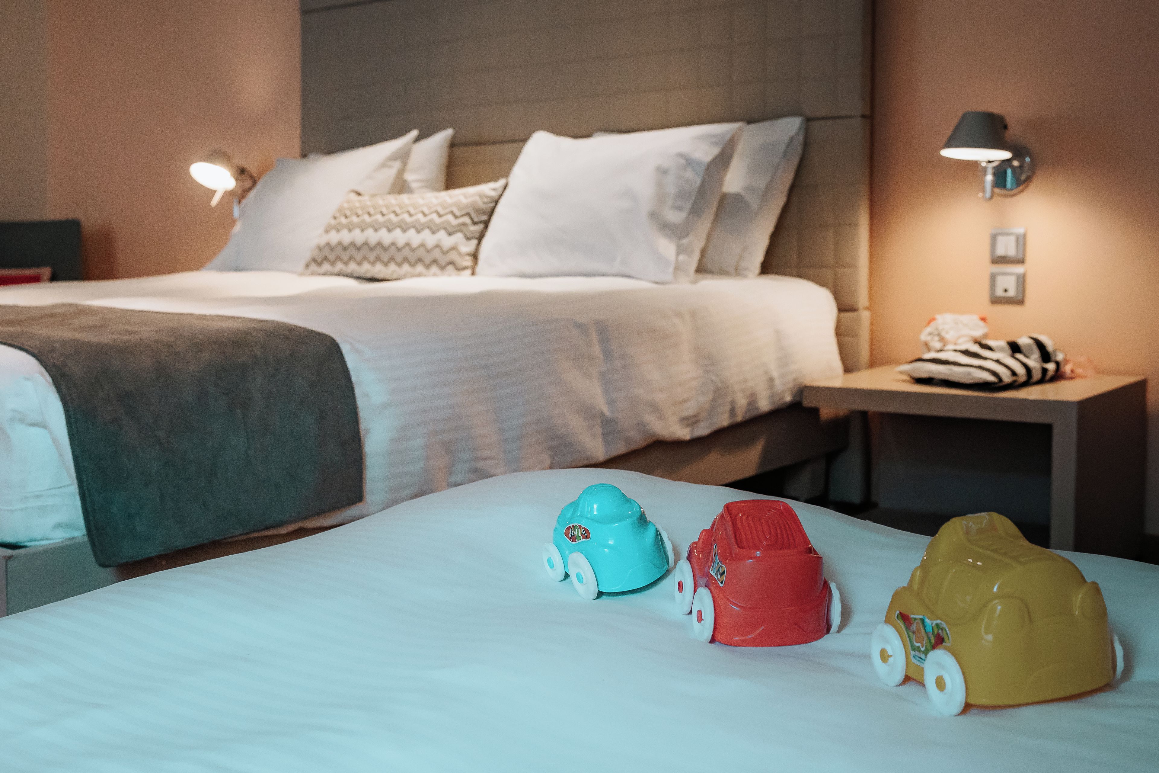 Una habitación de hotel con una cama, almohadas, una mesita de noche con lámpara y una luz empotrada en la pared.