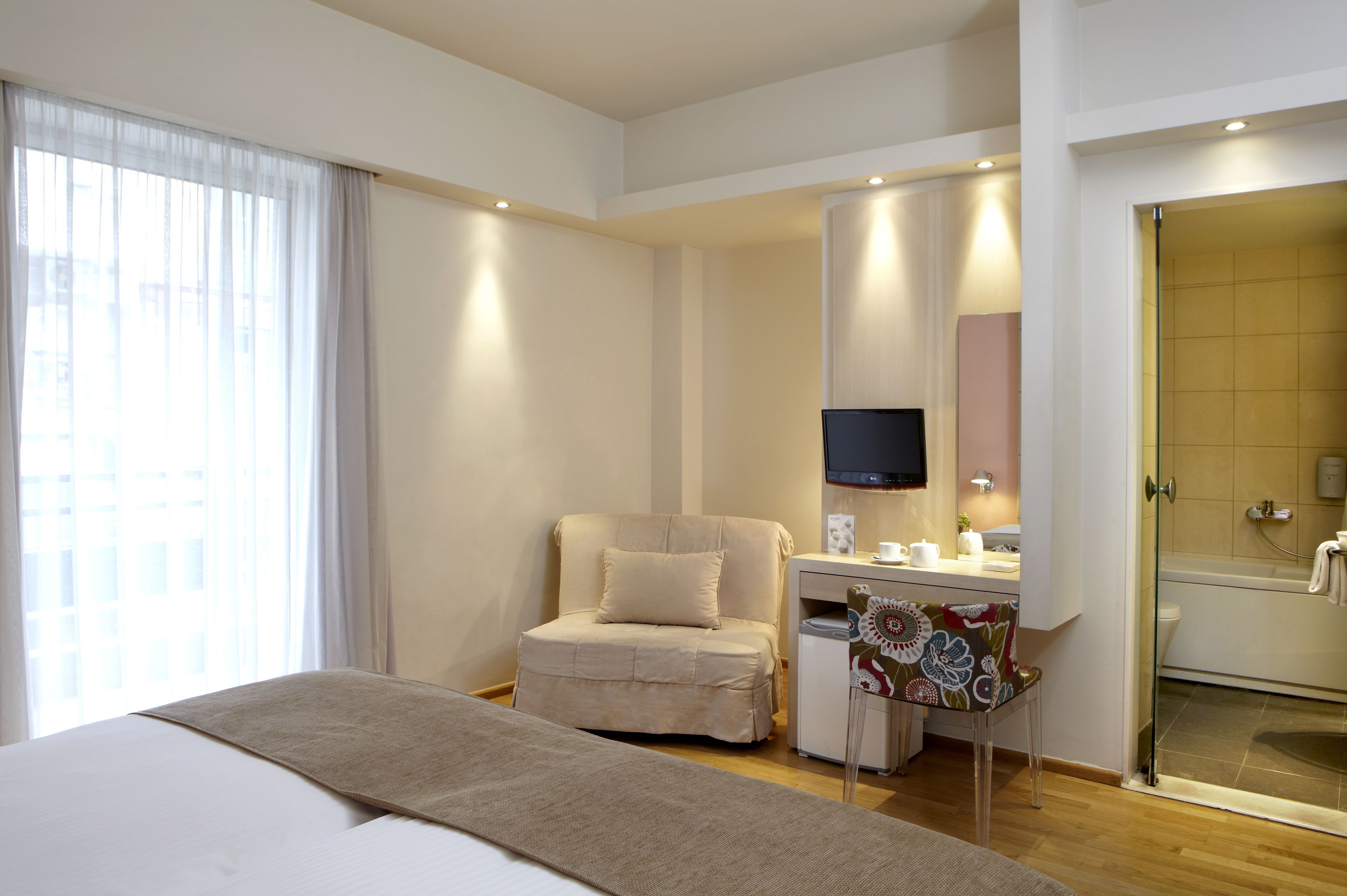 A hotel room with a bed, a desk with a chair, a television, a shower, and a window with curtains.