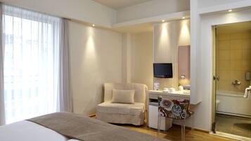 A hotel room with a bed, a desk with a chair, a television, a shower, and a window with curtains.