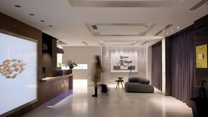 Un vestíbulo de hotel moderno con un mostrador de recepción, un cuadro abstracto de gran tamaño, una zona de estar y una planta.