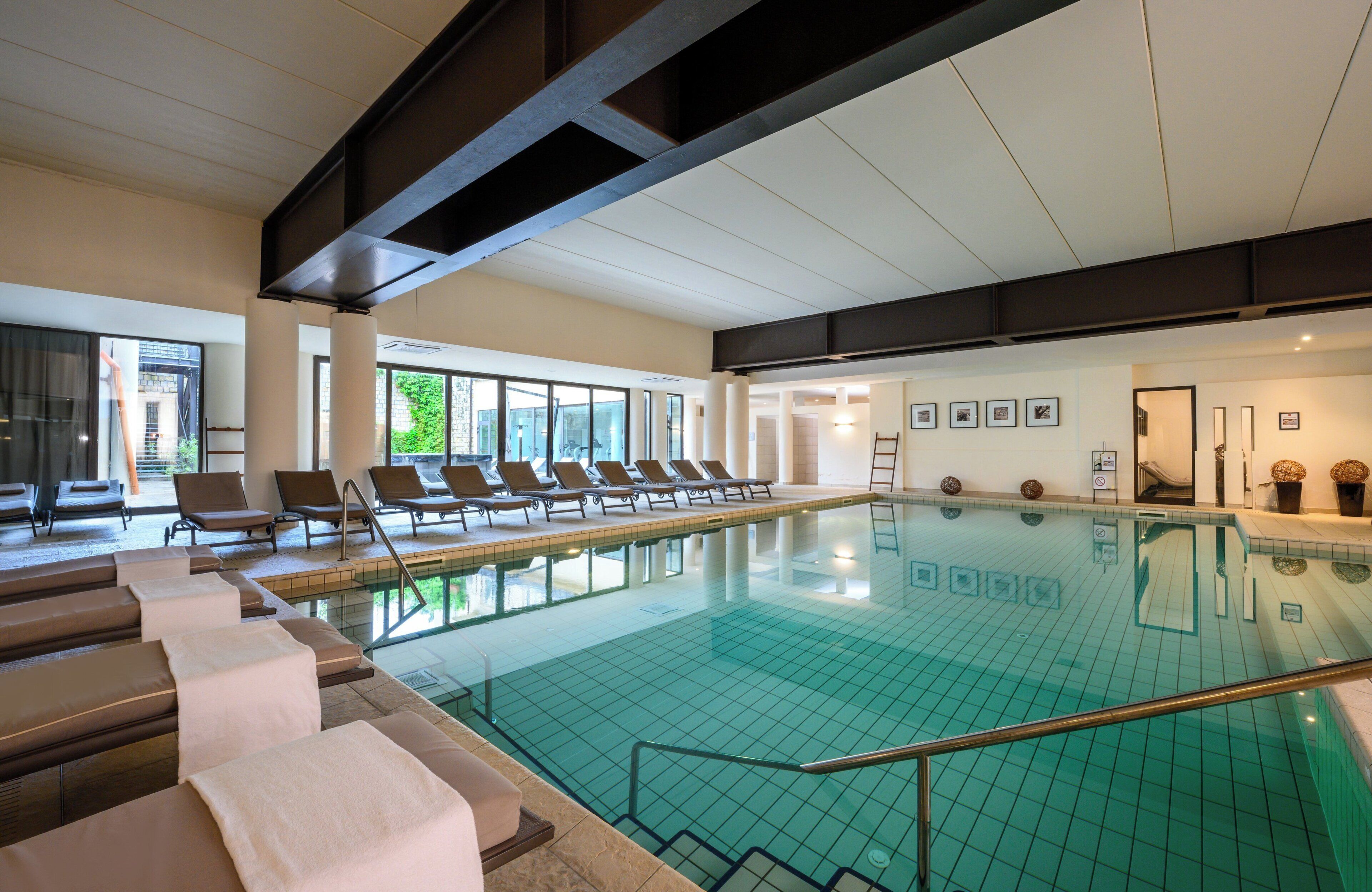 Uma piscina interior ampla com espreguiçadeiras e chão em azulejos.