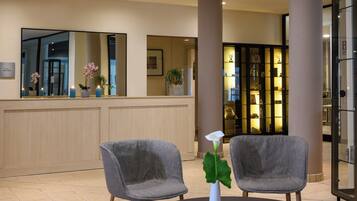 A reception area with two grey chairs, a white vase with a single white flower, and a reception desk with a mirror above it.