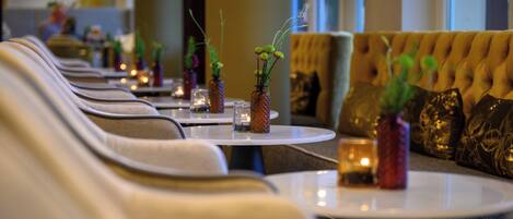 A row of round tables with vases of greenery, a tufted sofa, and a warm ambiance in a dining area.