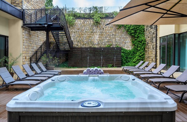 A hot tub with a wooden deck, surrounded by lounge chairs, a staircase, and a stone wall with greenery. - Leonardo Hotel Lago di Garda – Wellness and Spa (Lazise)