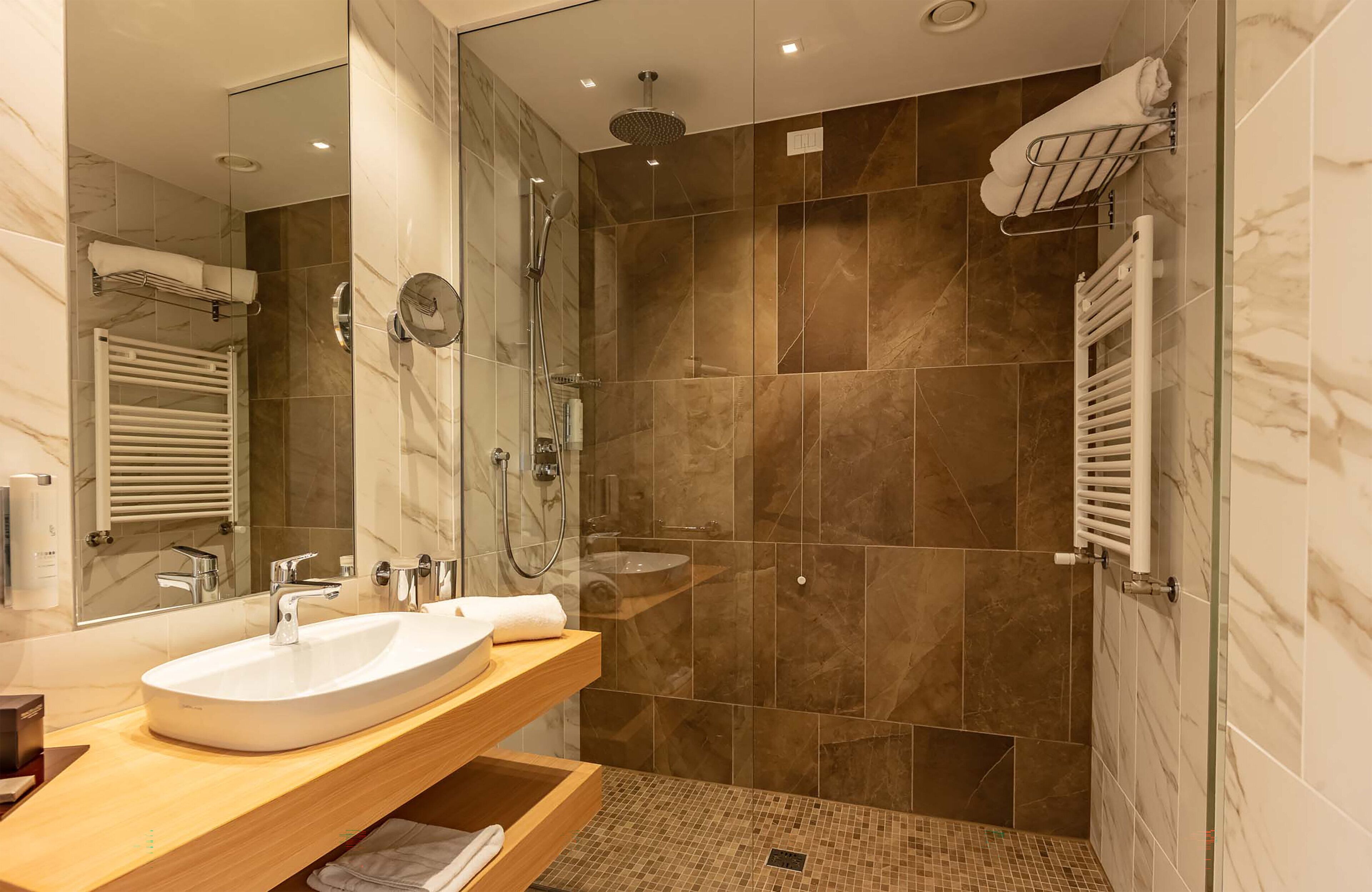 Un baño moderno con un lavamanos grande, dos espejos, una ducha con puerta de cristal y un perchero para toallas.