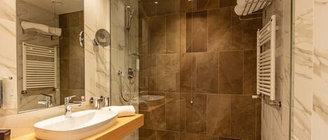 Un baño moderno con un lavamanos grande, dos espejos, una ducha con puerta de cristal y un perchero para toallas.