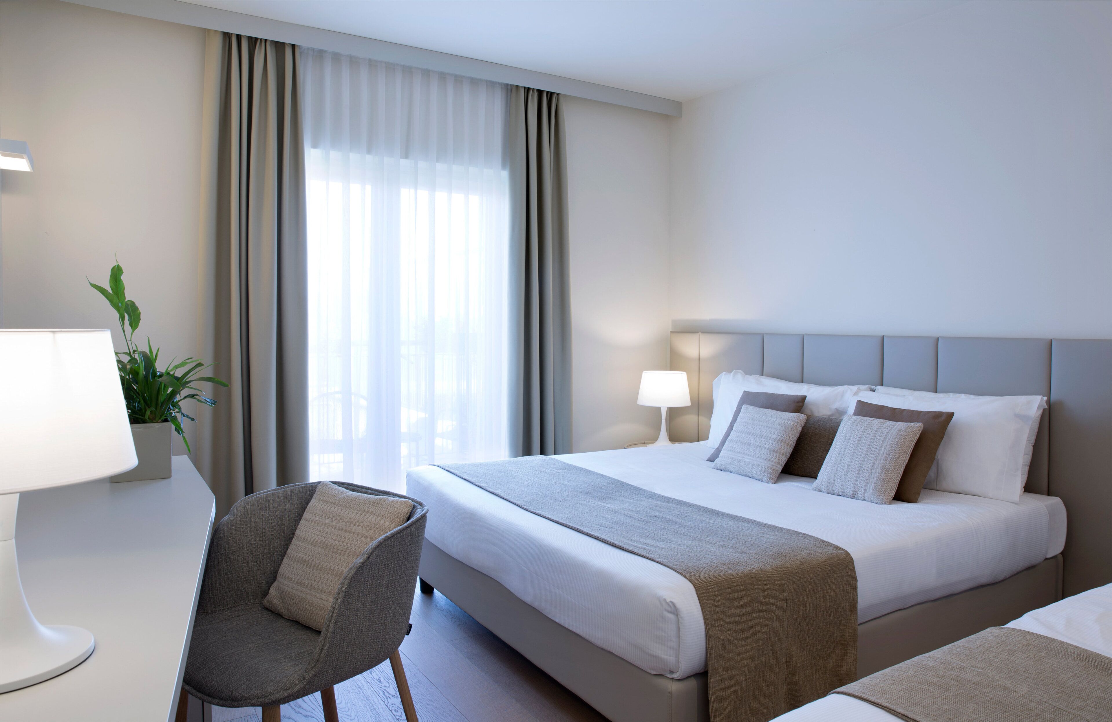 Una habitación de hotel con una cama, una silla, una lámpara y una planta.