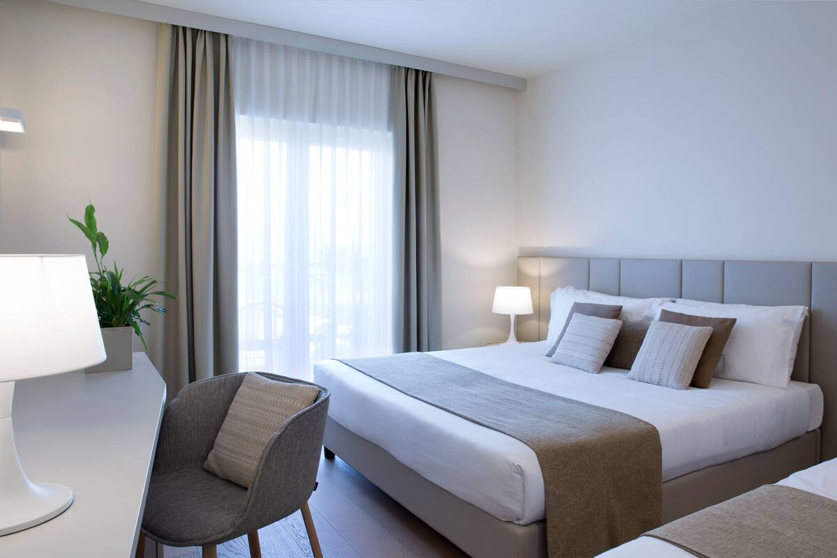 Une chambre d’hôtel avec un lit, une chaise, une lampe et une plante.