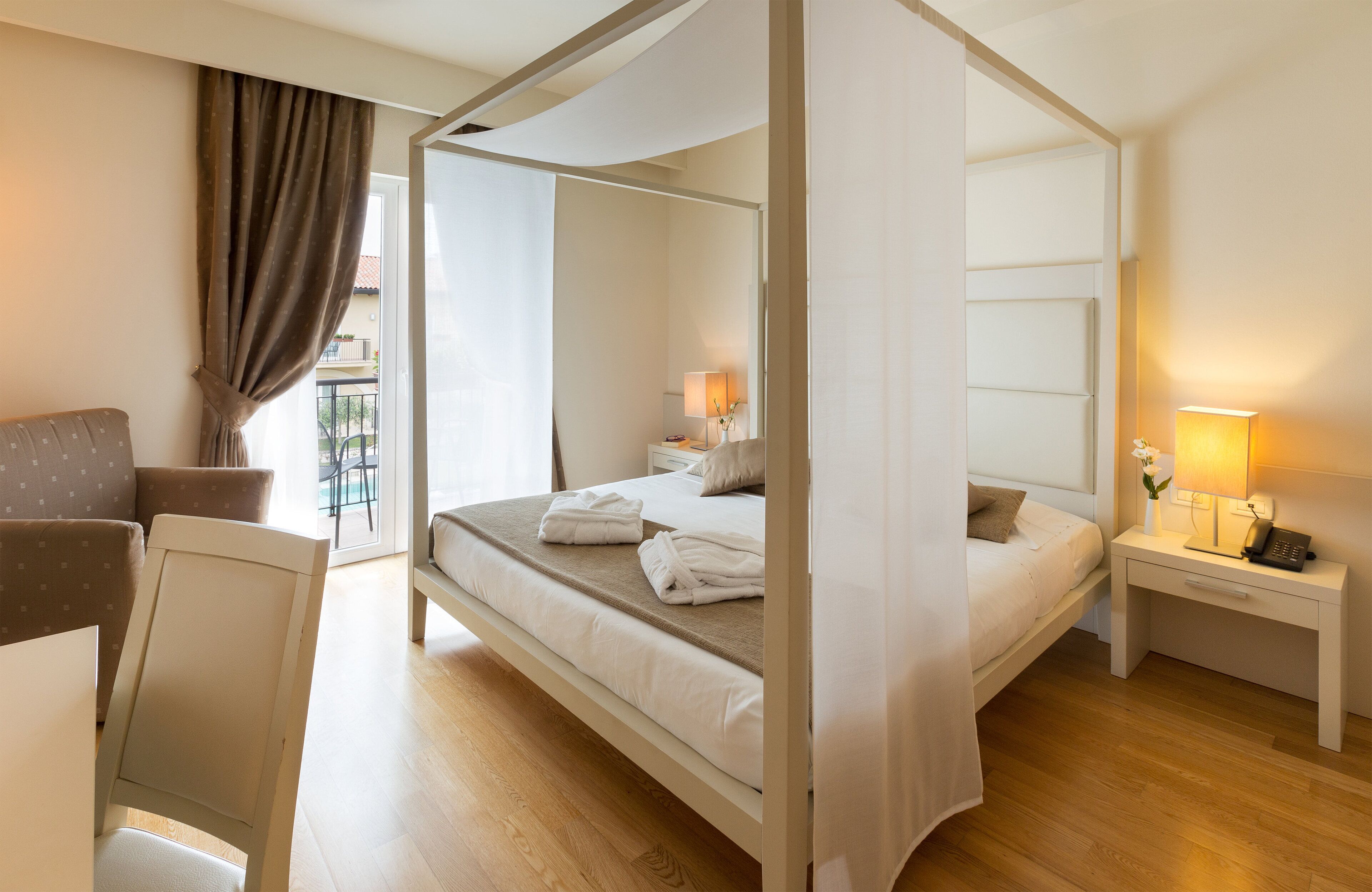A four-poster bed with white linens, a bedside table with a lamp, and a chair.