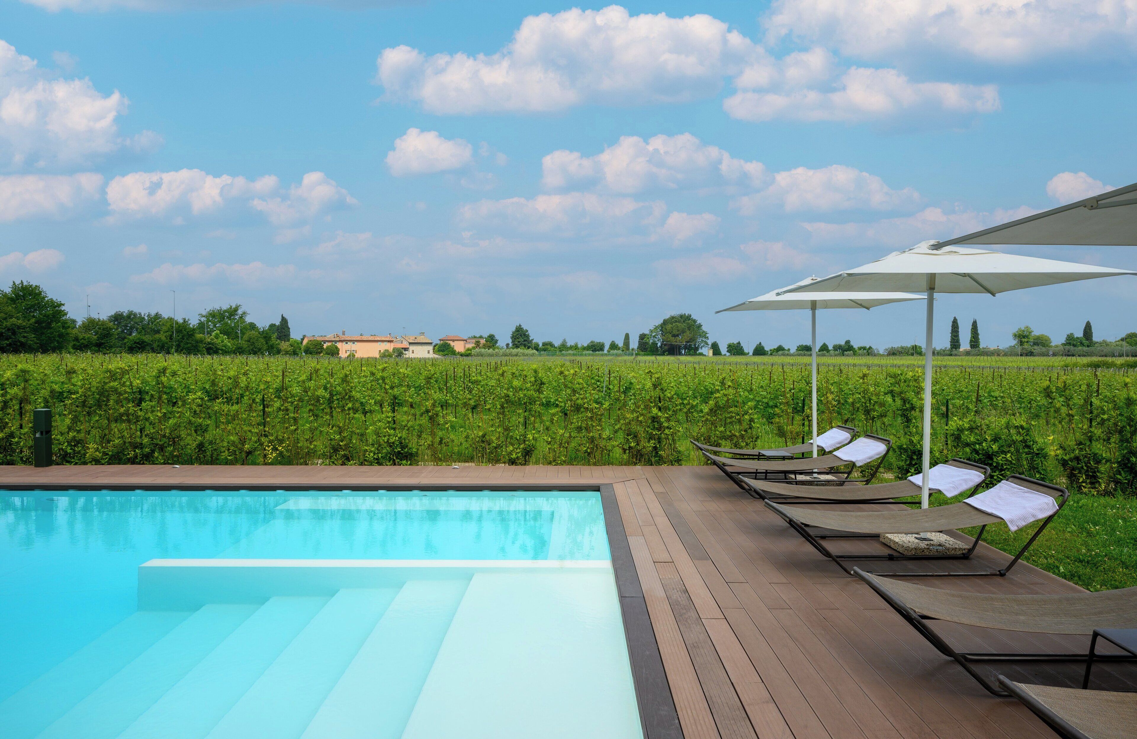 Ein Swimmingpool mit Liegestühlen und Sonnenschirmen, umgeben von viel Grün und blauem Himmel.