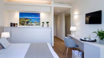 A modern hotel room with a large bed, a desk with a chair, a flat-screen TV, and a painting of a coastal landscape.