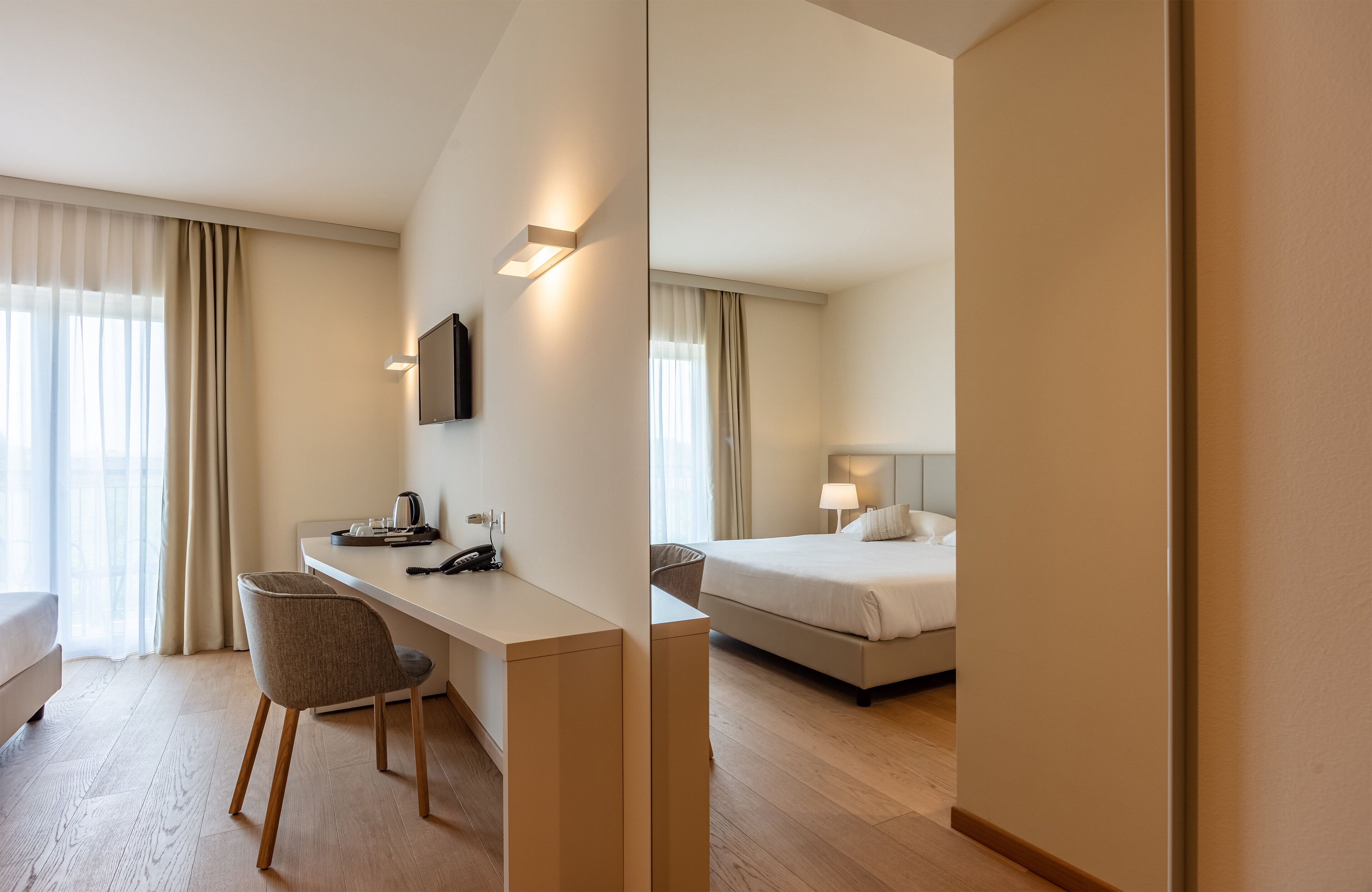 Een hotelkamer met een bed, een bureau, een stoel en een aan de muur bevestigde televisie.