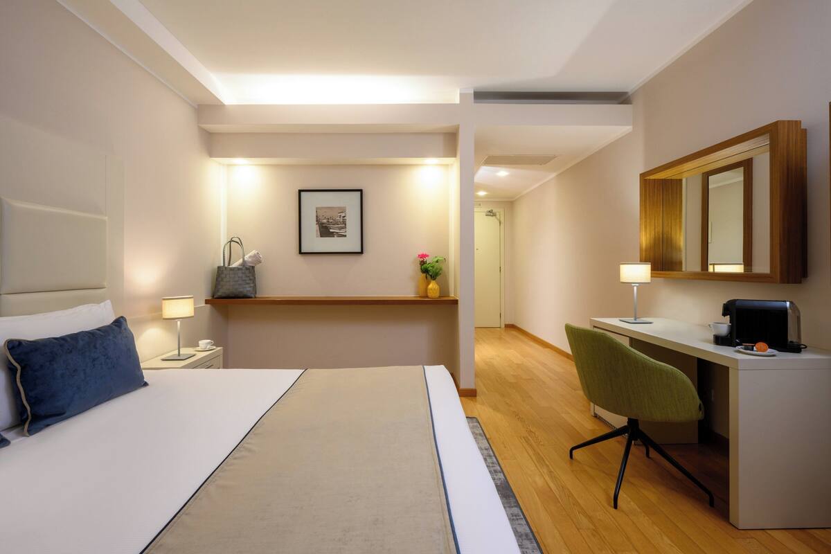 Une chambre d’hôtel avec un lit, un bureau, une chaise et un miroir.