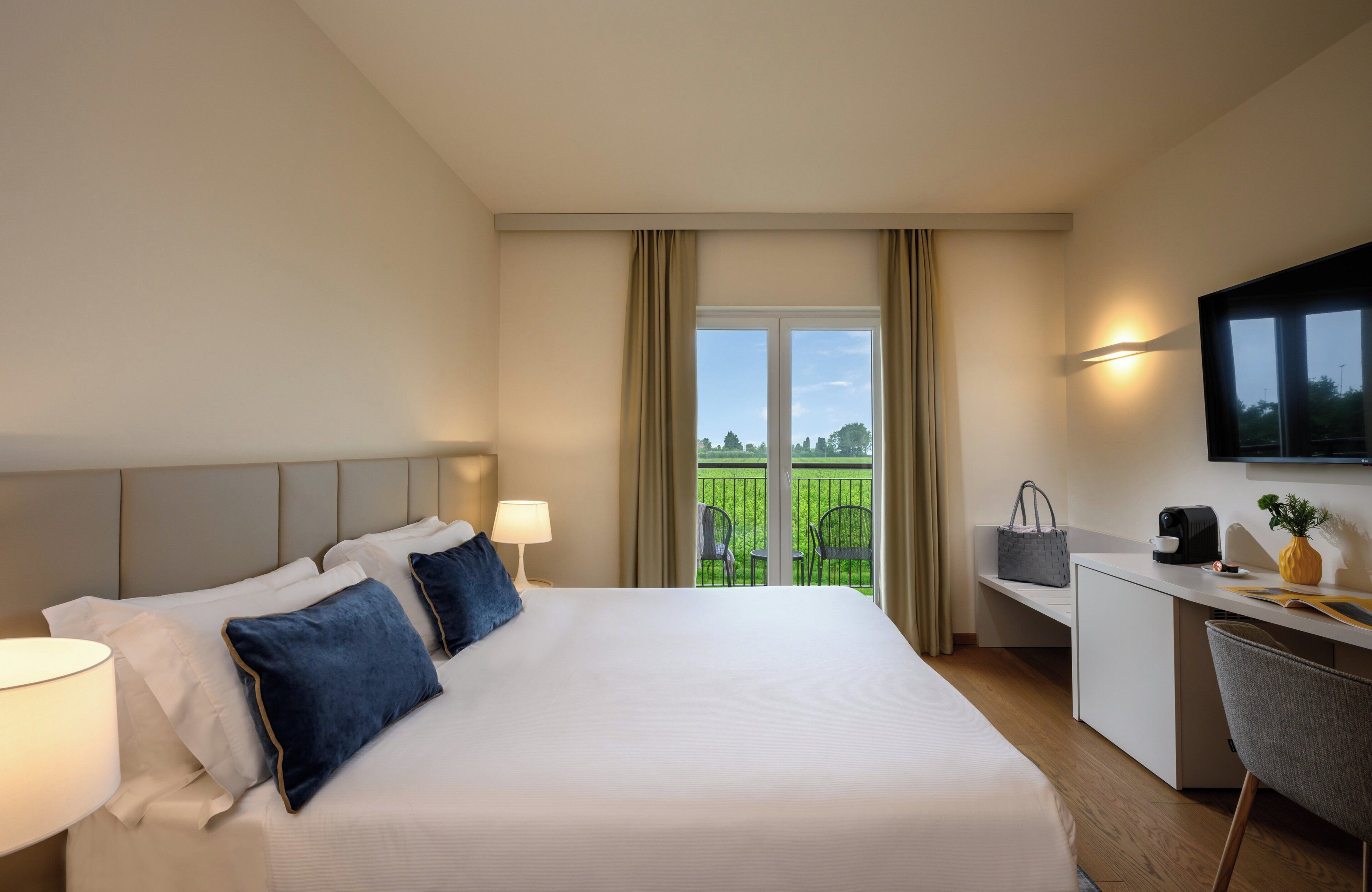 Une chambre d’hôtel avec un grand lit, un bureau, une chaise, une télévision et un balcon équipé de chaises.