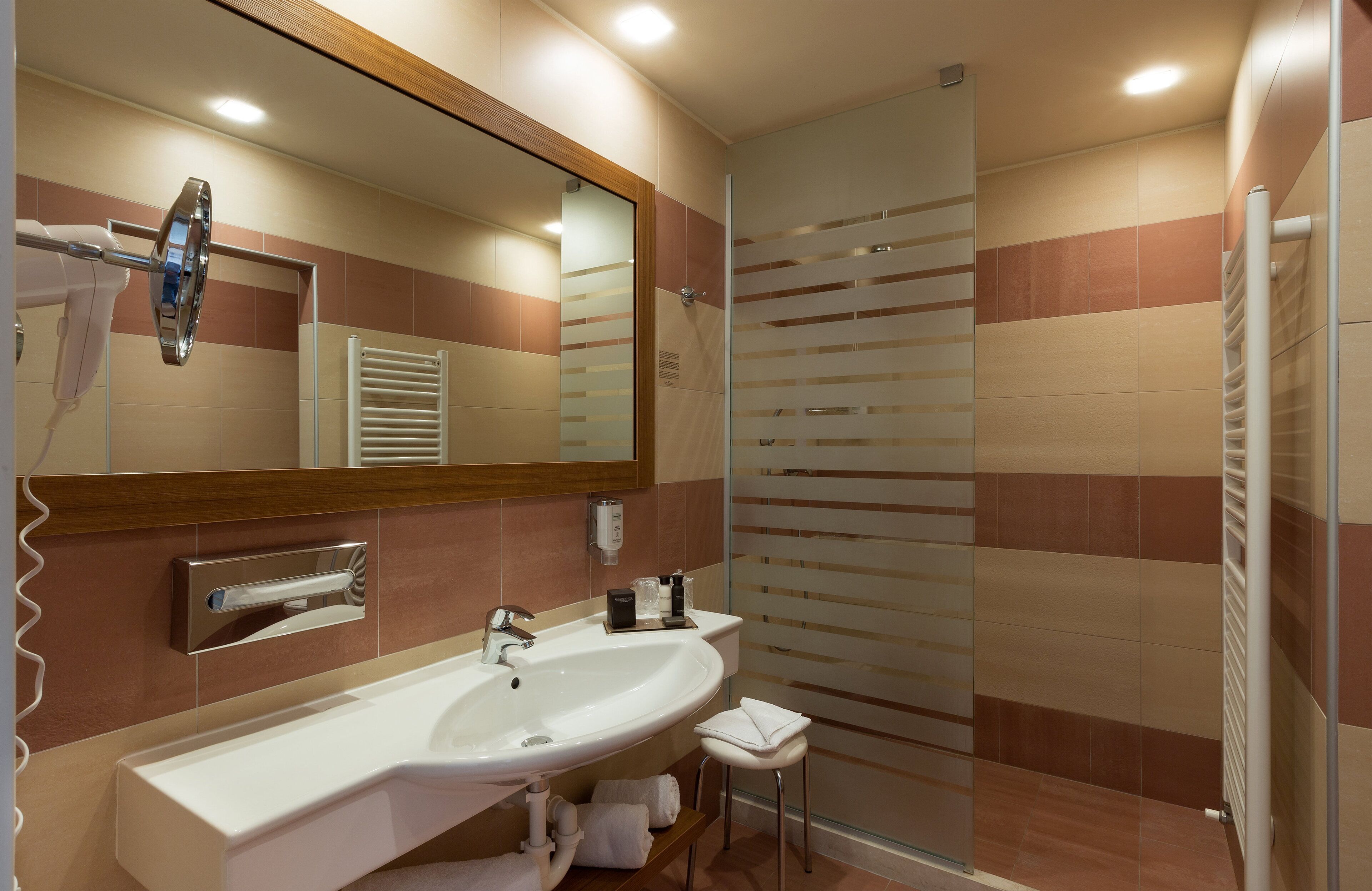 Un baño moderno con un espejo grande, dos lavamanos, un perchero para toallas y un box de ducha de vidrio.
