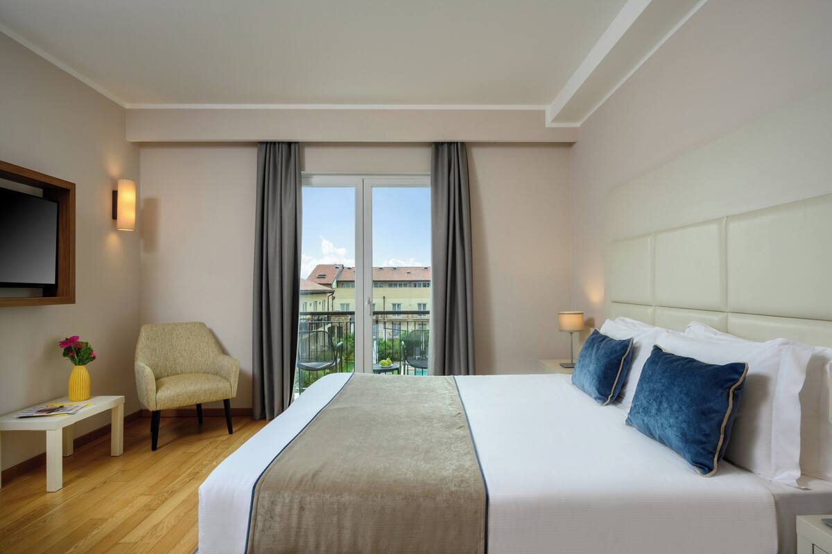 A hotel room with a large bed, a chair, a small table, and a TV on the wall.