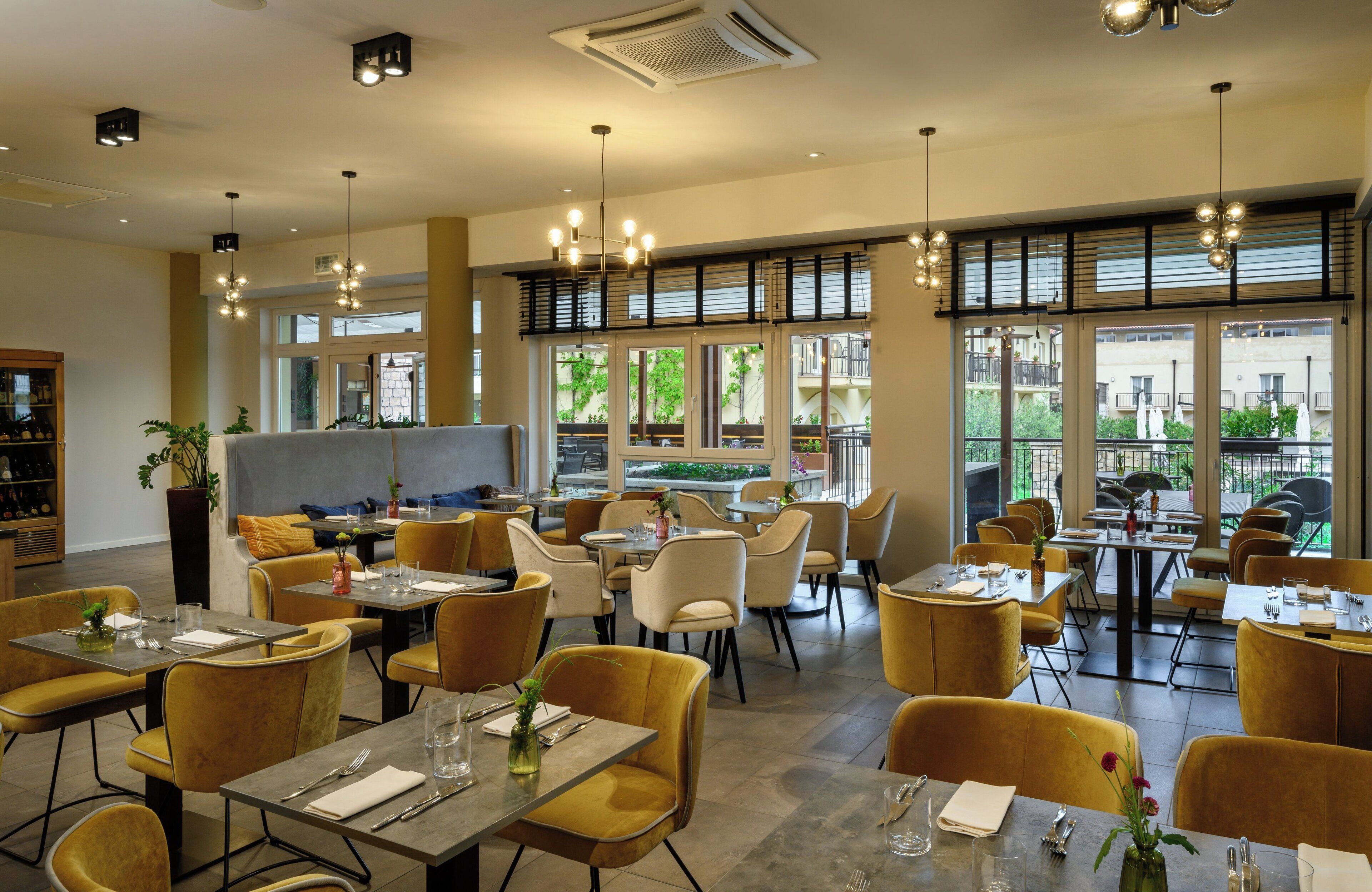 A restaurant with yellow chairs and tables, large windows, and hanging lights.