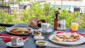 Mesa de café da manhã com pratos de comida, uma xícara de café e um copo de suco de laranja, com vista para a piscina.