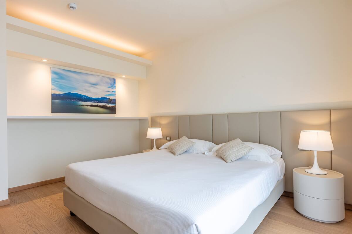 Une chambre d’hôtel moderne avec un grand lit, deux tables de chevet avec des lampes, un tableau accroché au mur et un plancher en bois.