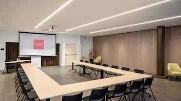 Un salón de conferencias con una larga mesa, sillas, una pantalla de proyector y un panel de pared de madera.
