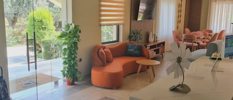 A modern living room with a sectional sofa, a flat-screen TV, a small round table, and a potted plant.