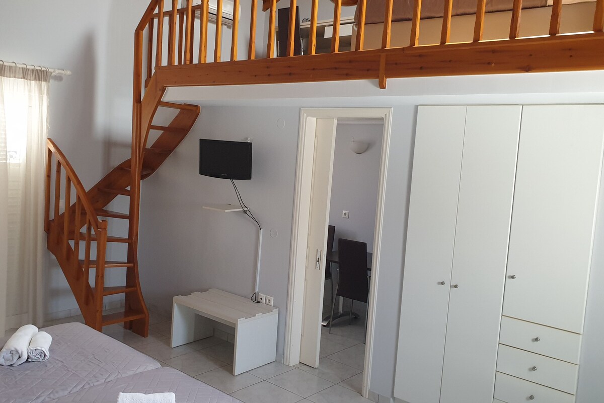 Un dormitorio con literas, una escalera de madera, un televisor montado en la pared, un escritorio y un armario.