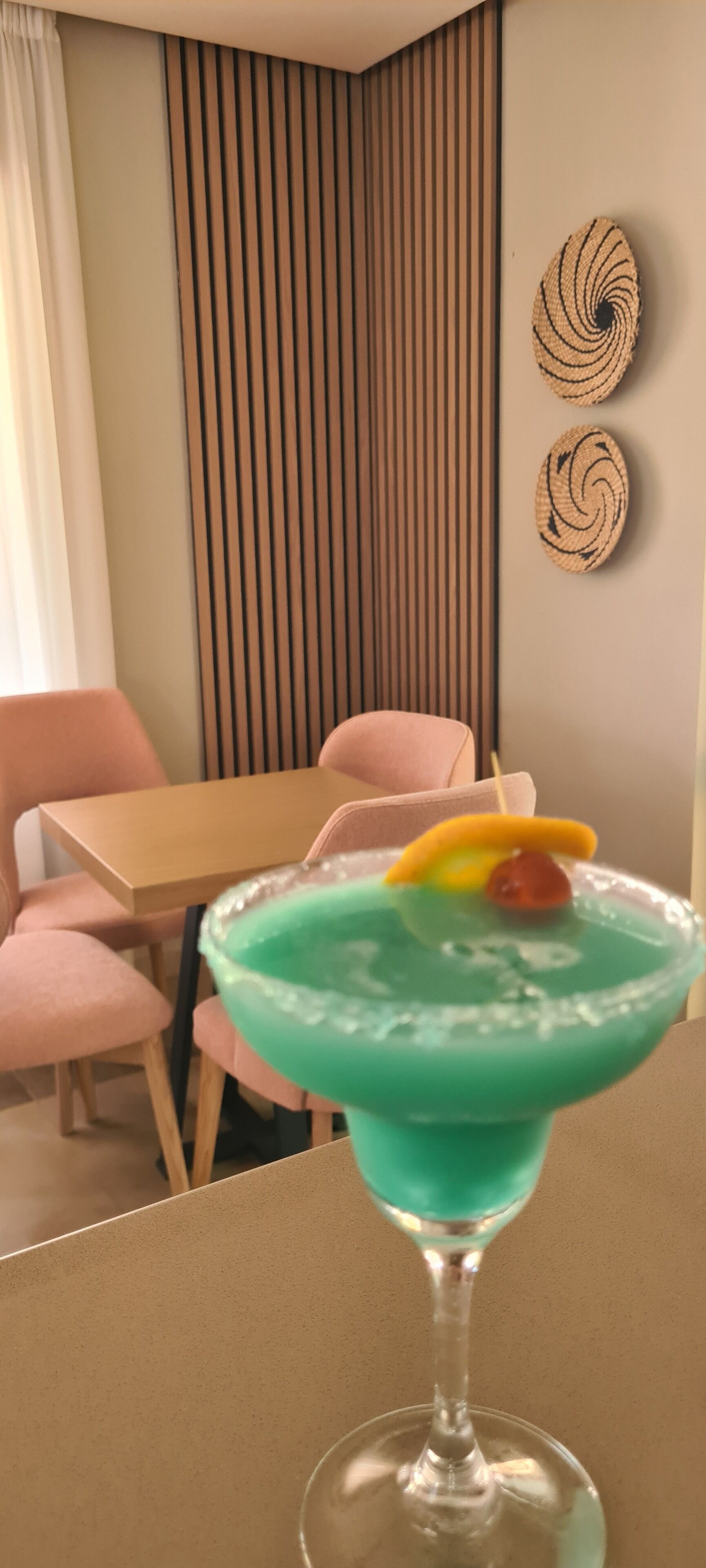 A room with a table and chairs, a green cocktail with a garnish, and decorative wall art.