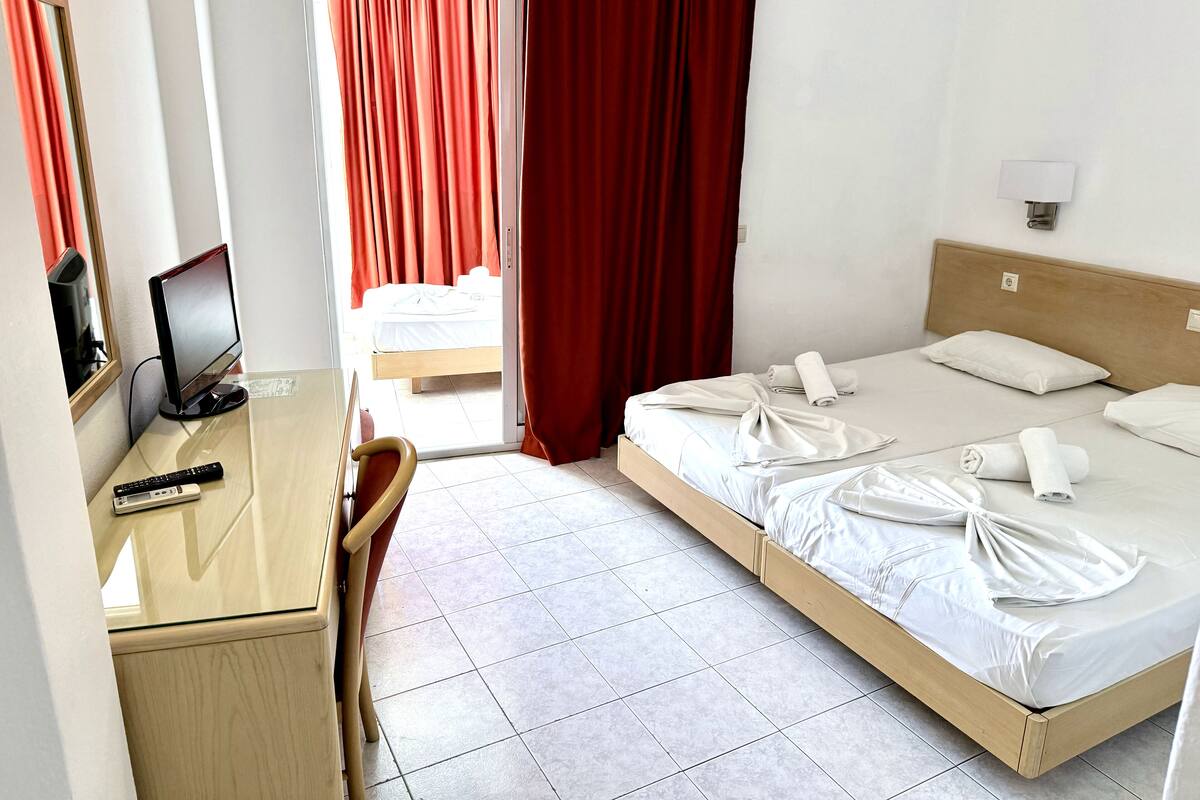 Una habitación de hotel con una cama, un escritorio, una silla, un televisor y una ventana con cortinas.