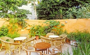 An outdoor patio with wicker furniture and a yellow wall. - Savoy City Hotel (Rhodes)