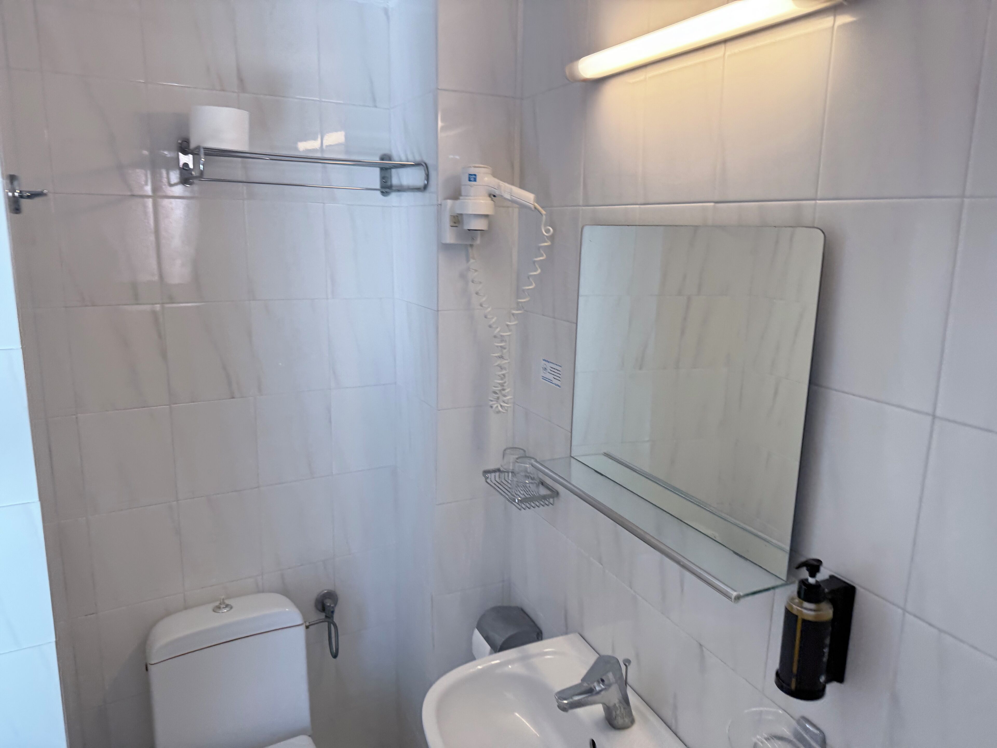 A bathroom with a toilet, sink, mirror, and towel rack.