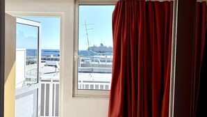 A room with a balcony, a window with red curtains, and a view of a cruise ship. - Savoy City Hotel (Rhodes)