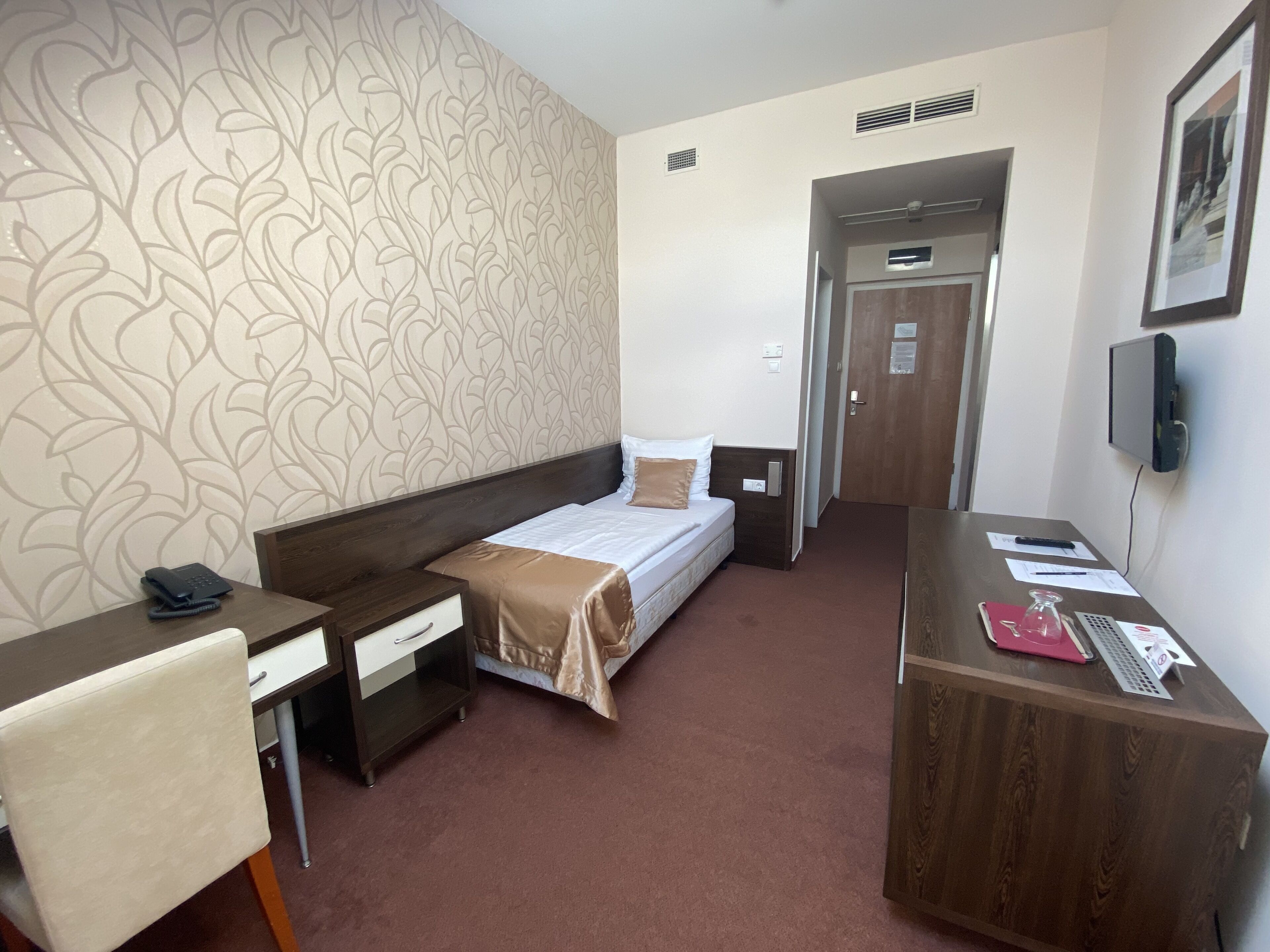A hotel room with a bed, a desk, a chair, a wardrobe, and a door leading to another room.