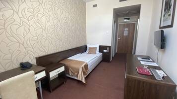 A hotel room with a bed, a desk, a chair, a wardrobe, and a door leading to another room.