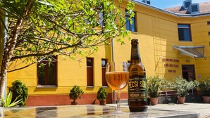A bottle of Pécsi Sör Premium Lager and a glass on a metal table outdoors with a yellow building in the background. - Boutique Hotel Sopianae (Pecs)