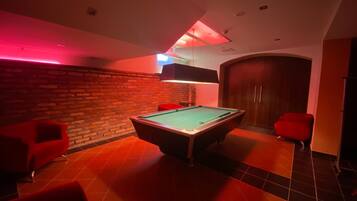 A billiards room with a pool table, red chairs, and a brick wall.