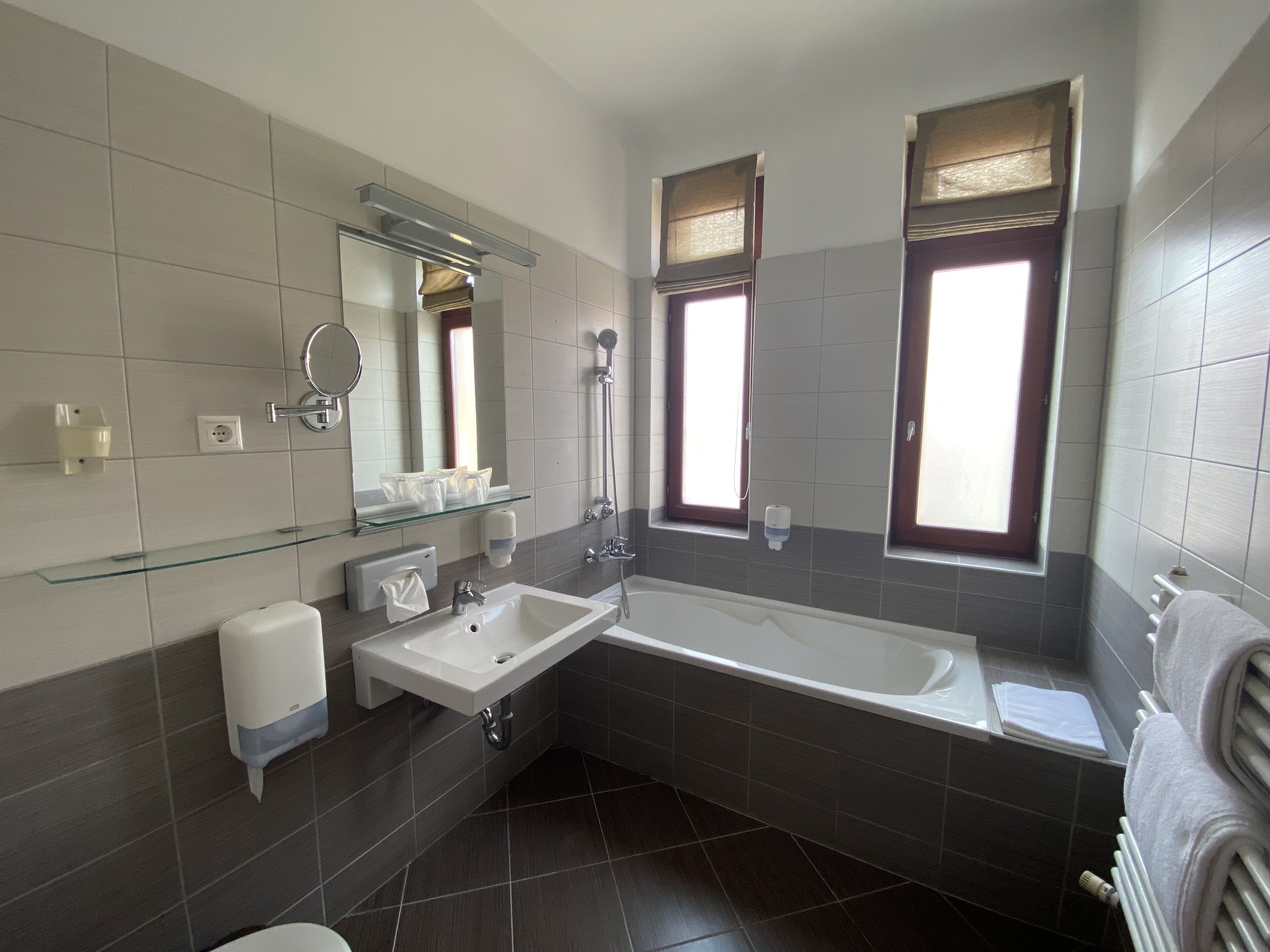 A modern bathroom with a glass shelf, a white sink, a bathtub, and a window with a view.