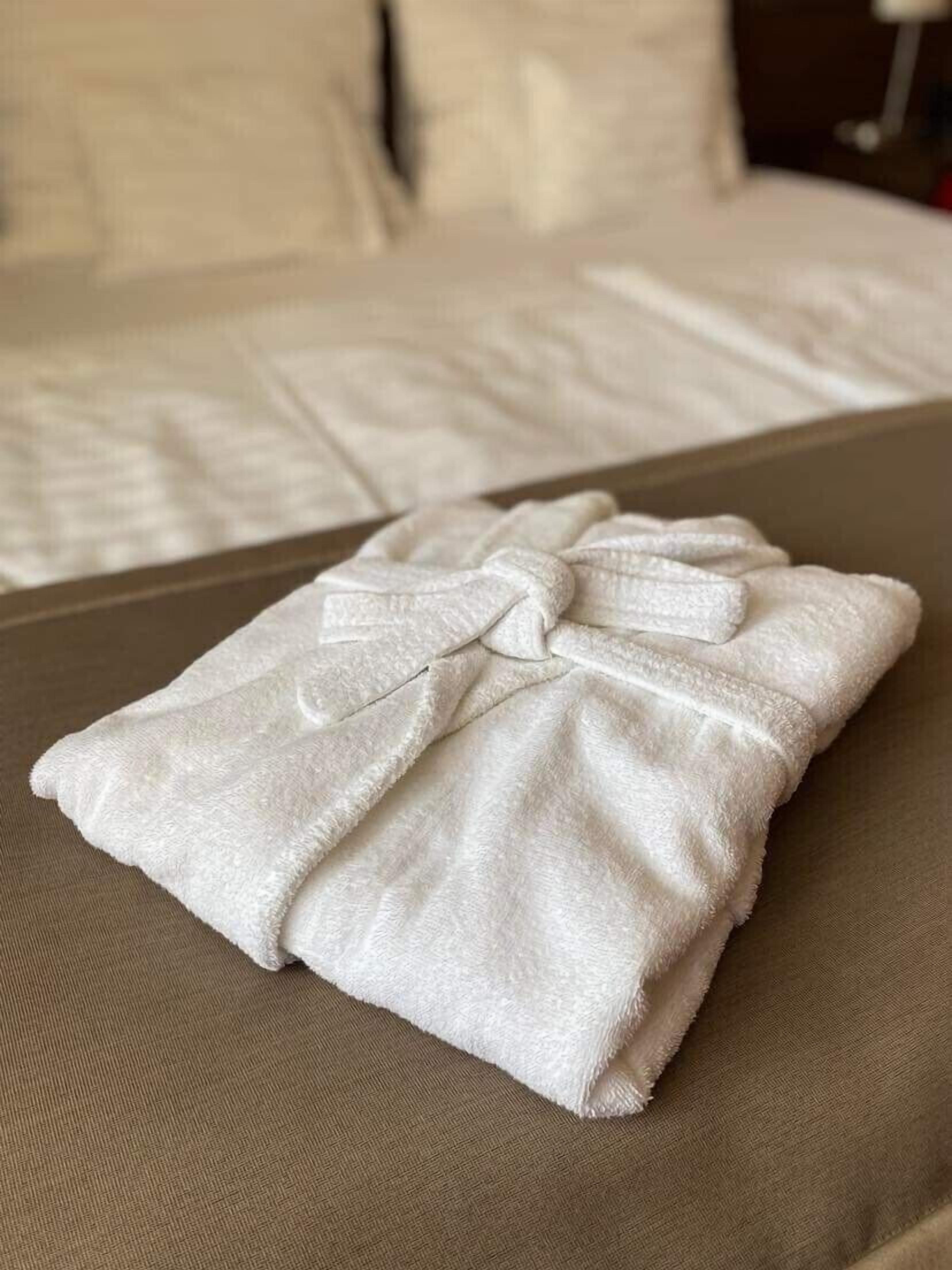 A neatly folded white towel on a brown fabric surface, likely a bed or couch.