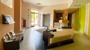 A hotel room with a bed, a desk, a small table, and a reception area with a counter and a window. - Boutique Hotel Sopianae (Pecs)