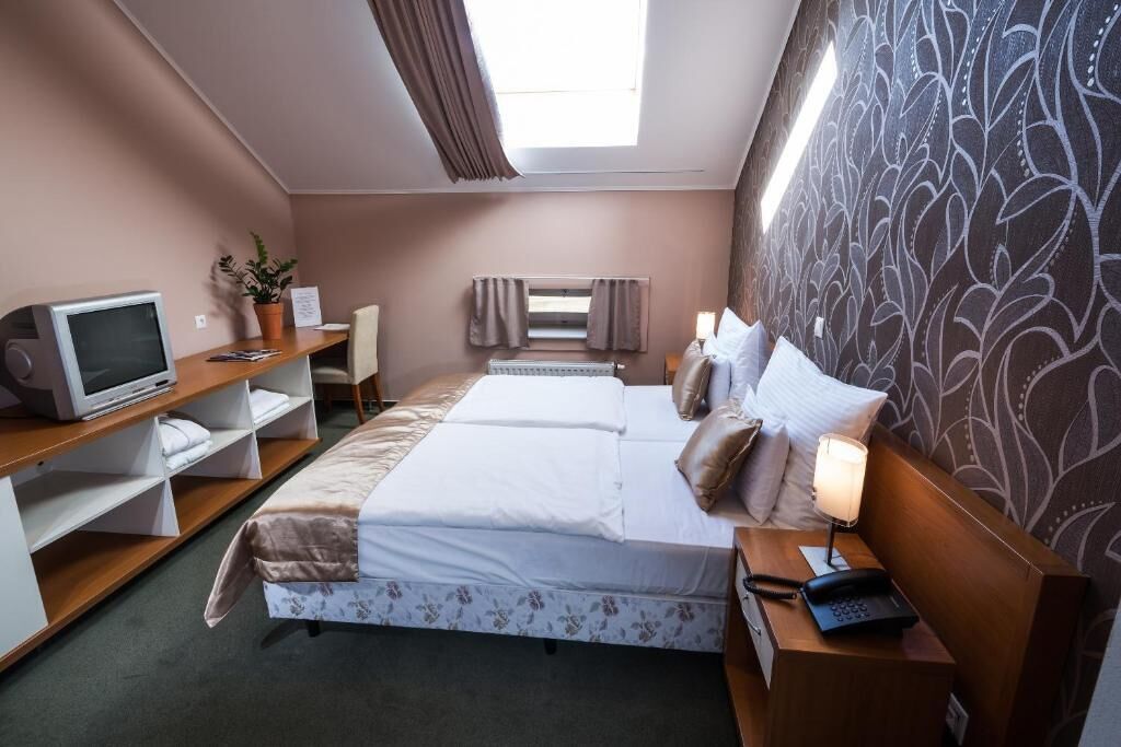 Una camera d'albergo con due letti, una scrivania con un computer, un tavolino con una lampada e una finestra con tende.