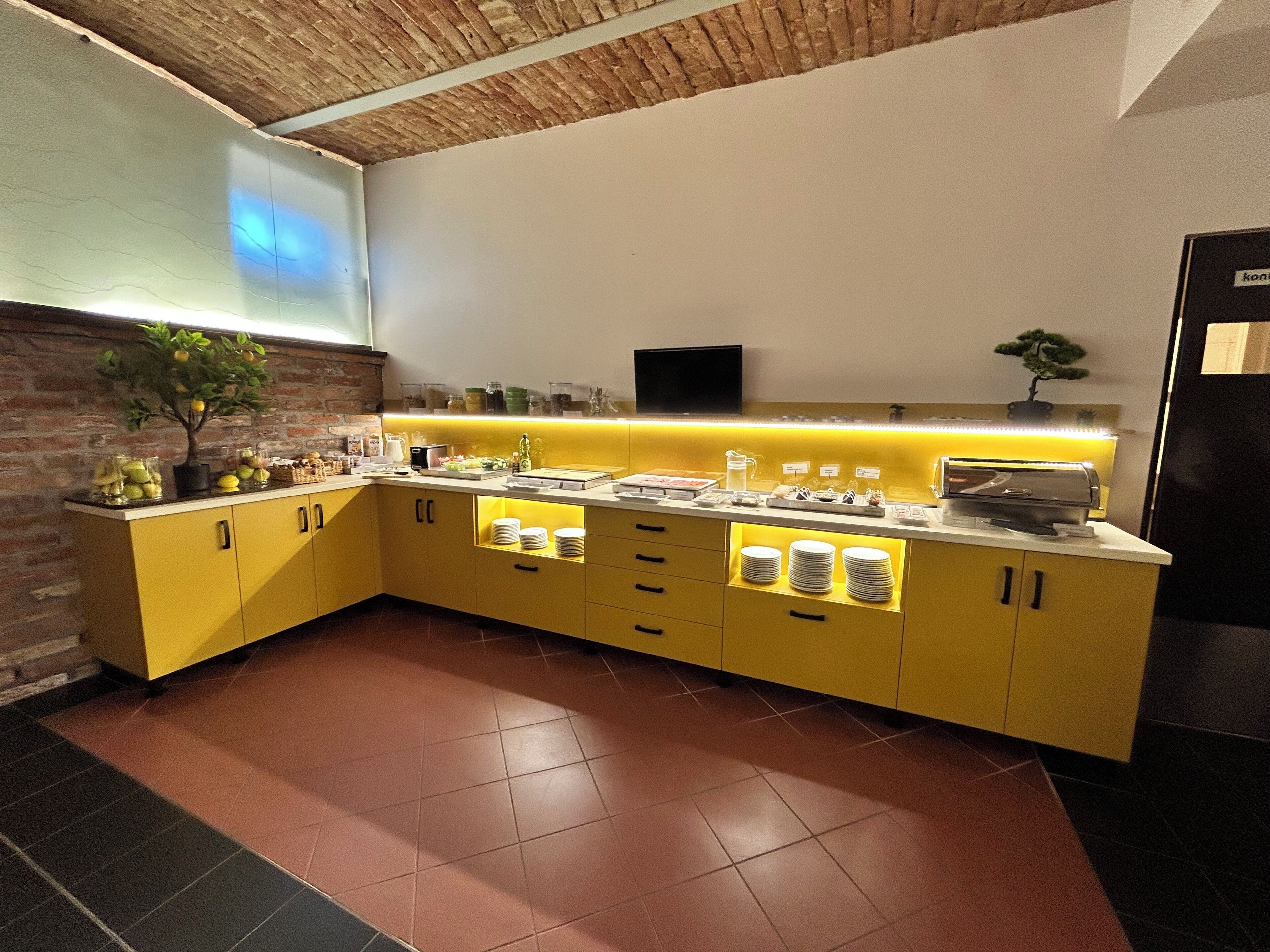 A modern kitchen with yellow cabinets, a brick accent wall, and a built-in TV.