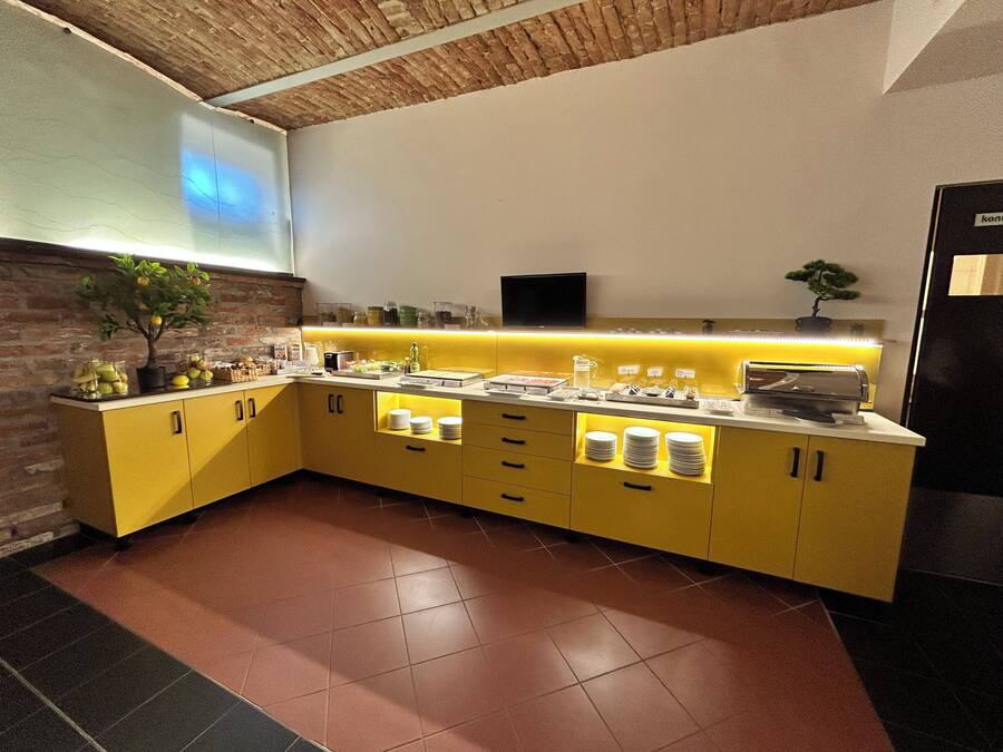 A modern kitchen with yellow cabinets, a brick accent wall, and a built-in TV.