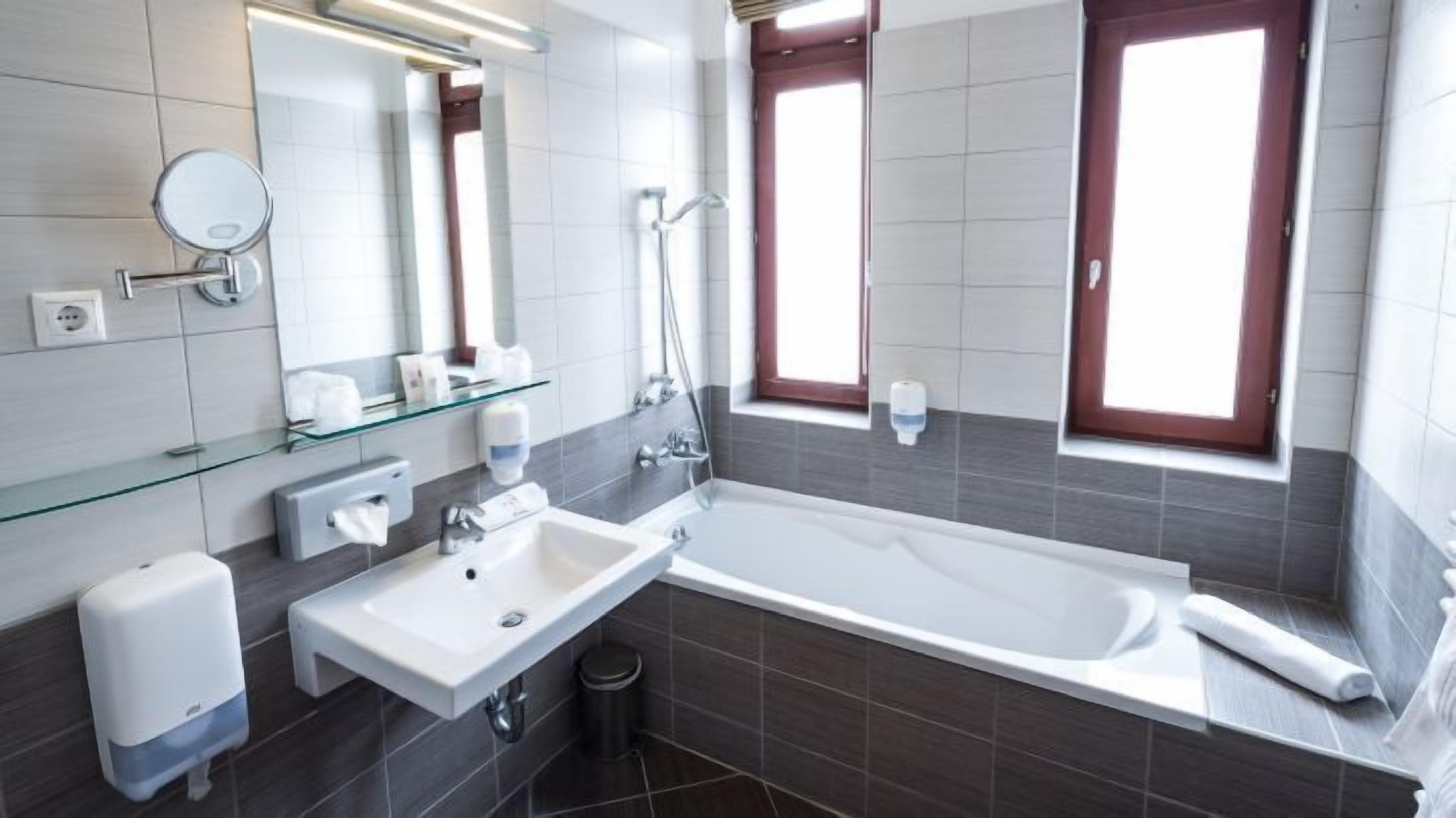 Une salle de bain moderne avec une baignoire, un lavabo, une étagère en verre et deux fenêtres.