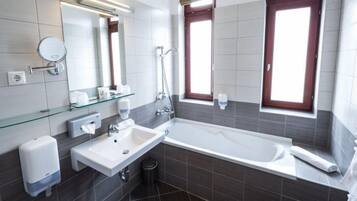 Une salle de bain moderne avec une baignoire, un lavabo, une étagère en verre et deux fenêtres.