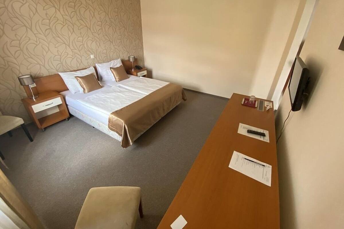 A hotel room with a bed, bedside tables, a desk, a chair, and a TV.