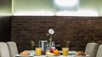 A breakfast setting with croissants, fruit, and orange juice on a table, with a brick wall and a flower in the background.