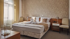 A hotel room with a large bed, two bedside tables, a chair, a desk, and a window with curtains. - Boutique Hotel Sopianae (Pecs)