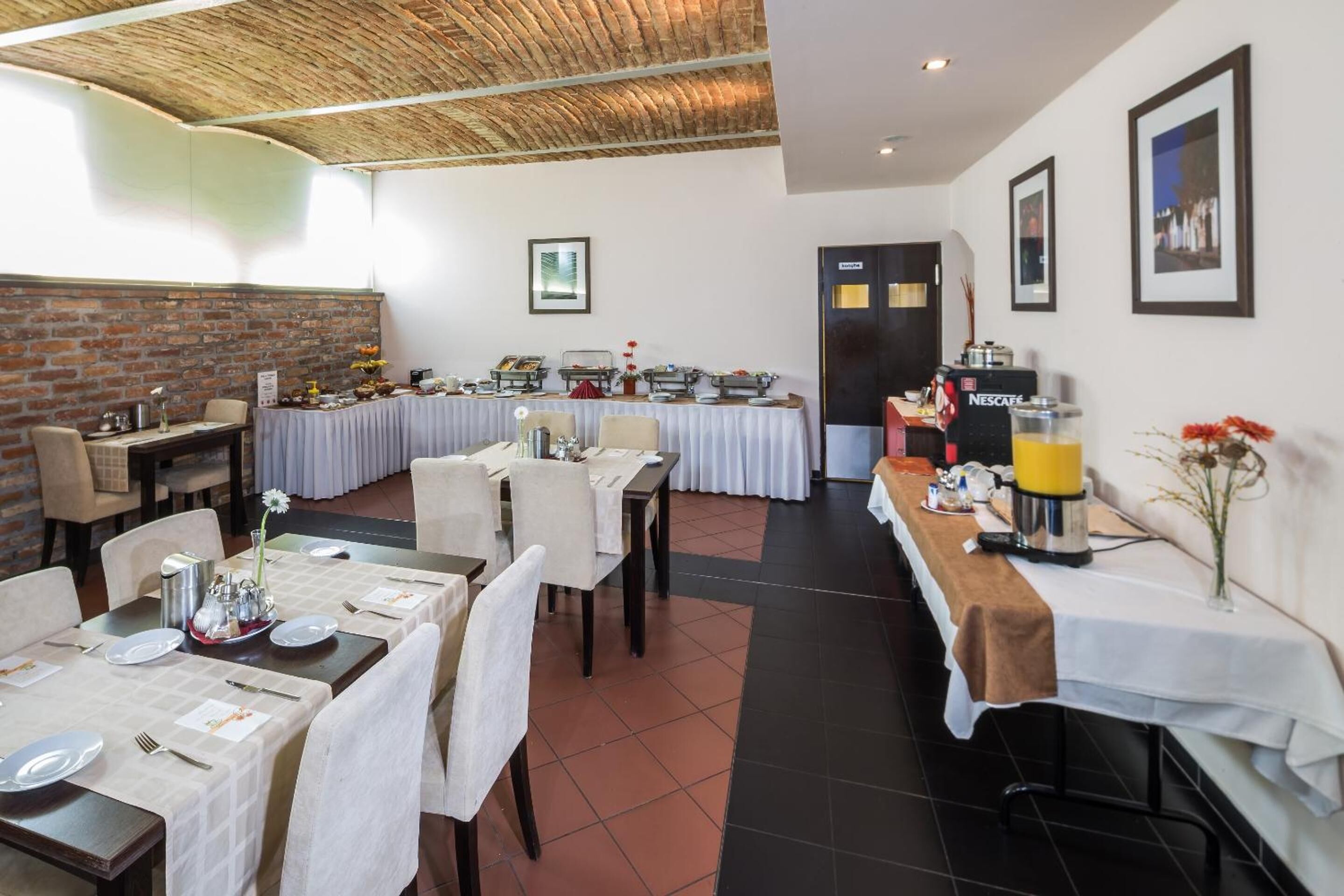 A dining area with multiple tables set for service, a brick wall, and framed pictures on the walls.