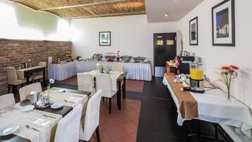 A dining area with multiple tables set for service, a brick wall, and framed pictures on the walls.