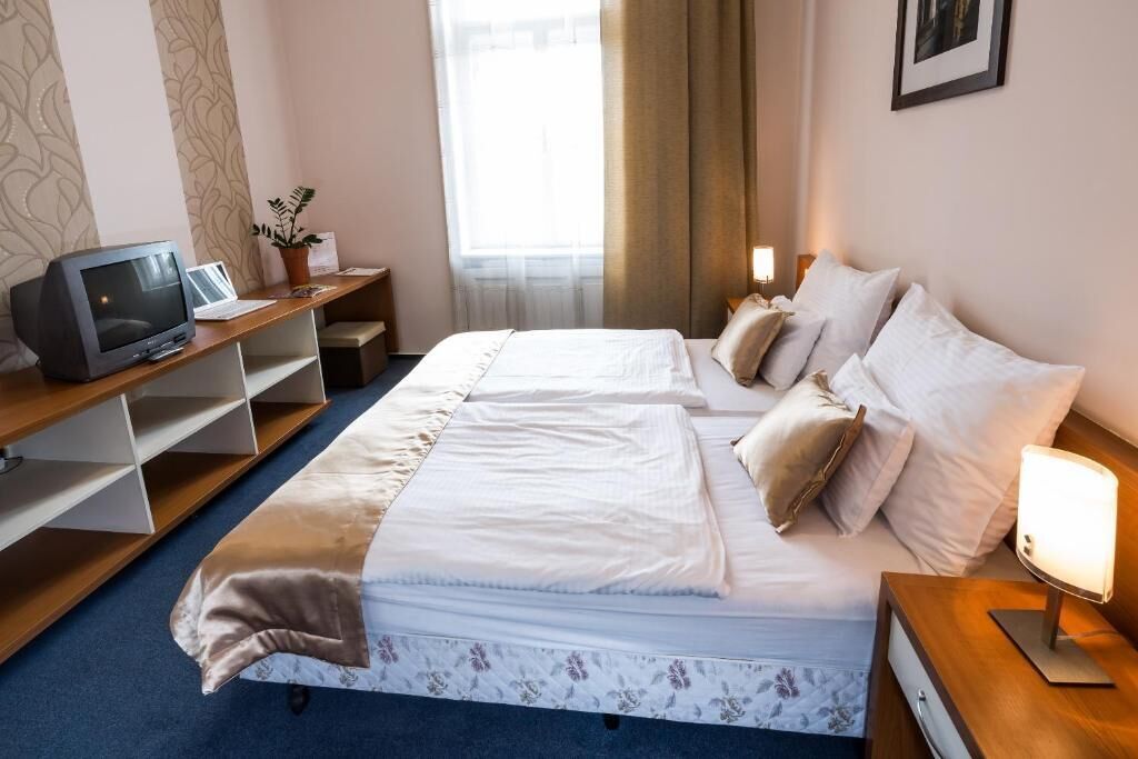 Ein Hotelzimmer mit zwei Betten, einem Schreibtisch mit Computer, einem Fernseher und einem Fenster mit Vorhängen.